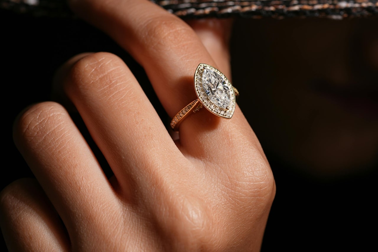A close-up of a woman’s hand wearing a distinctive engagement ring with a marquise cut center stone.