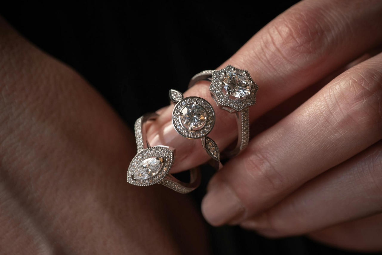 A close-up of a hand holding three intricate diamond rings.