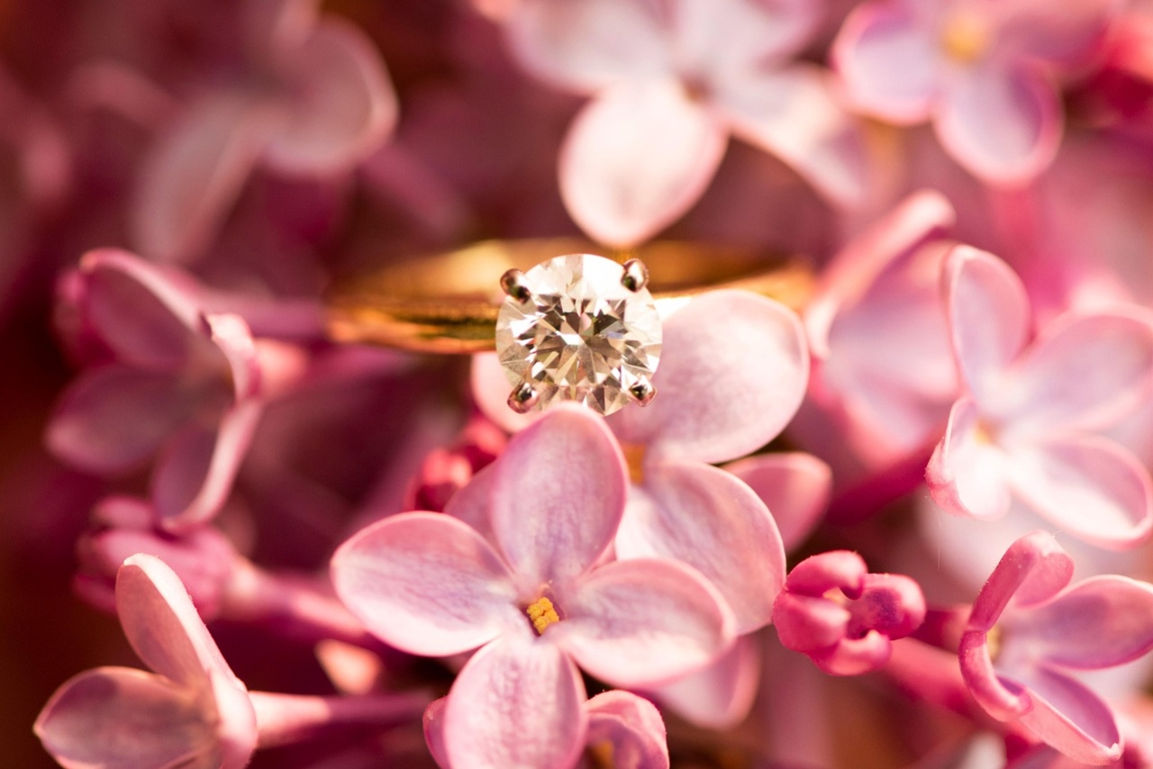 A classic solitaire diamond engagement ring with a yellow gold band is displayed among soft pink flowers.