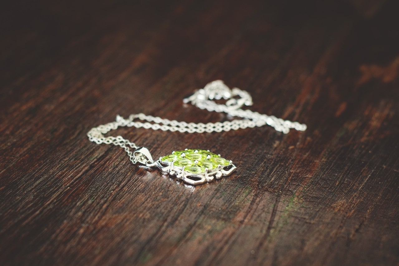 A white gold peridot necklace lying on a hardwood surface.