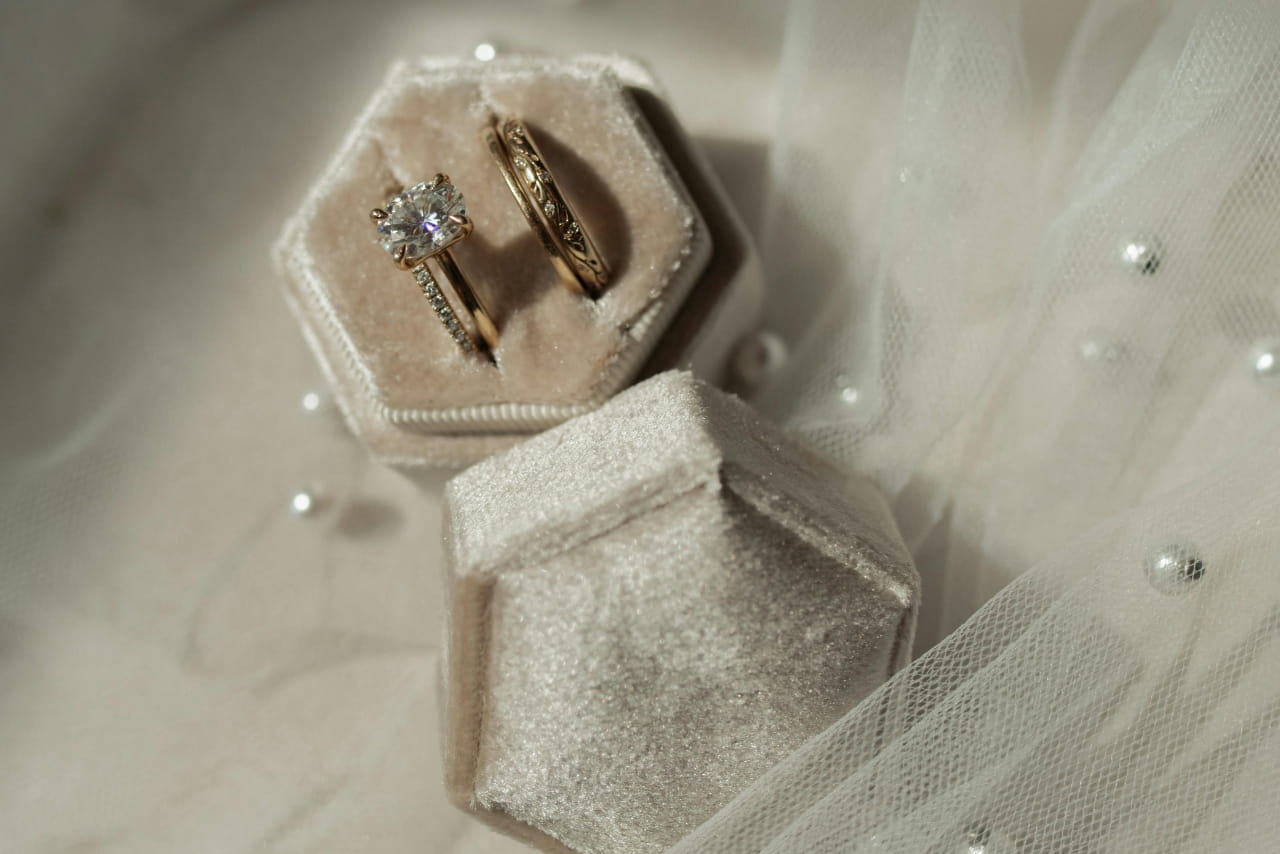 A cream velvet ring box with a yellow gold engagement ring and 3 yellow gold wedding bands.