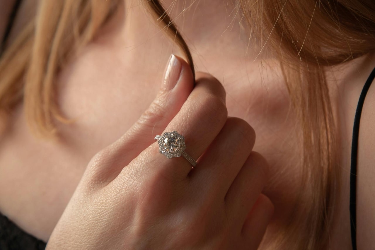 A woman with red hair holding on to a strand of it, showcasing her stunning engagement ring.