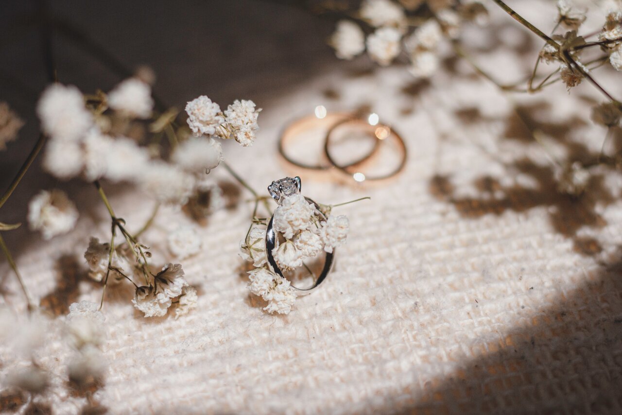 A white gold diamond ring on a piece of fabric with two yellow gold wedding bands in the background.