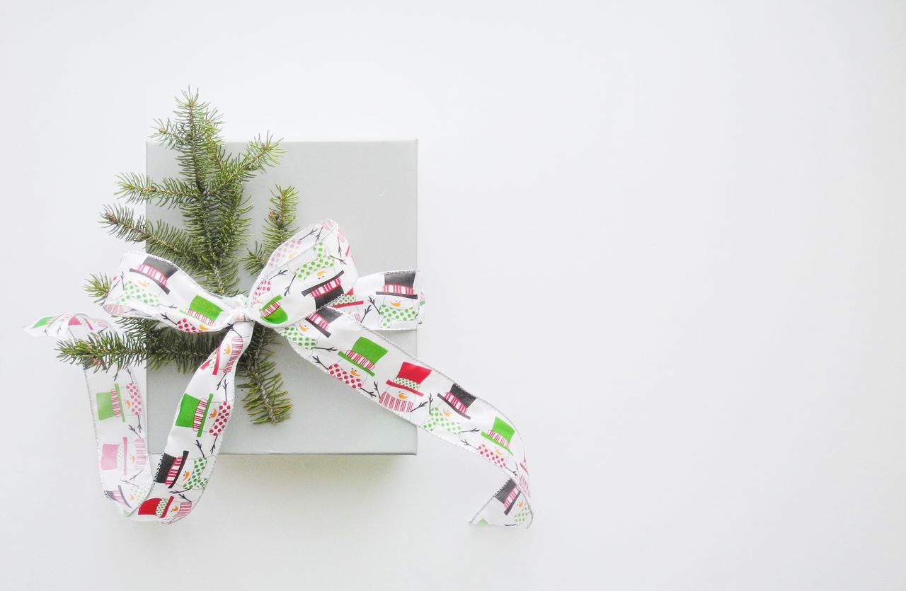A small, white gift box tied shut with a snowman-adorned ribbon with a decorative pine tree twig