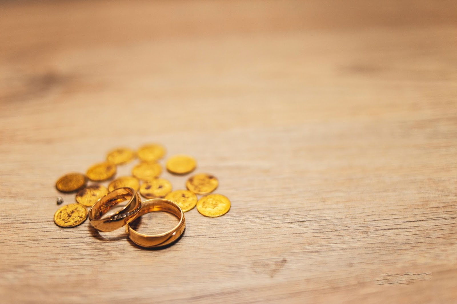 Two yellow gold wedding bands sit on a table among a pile of coins