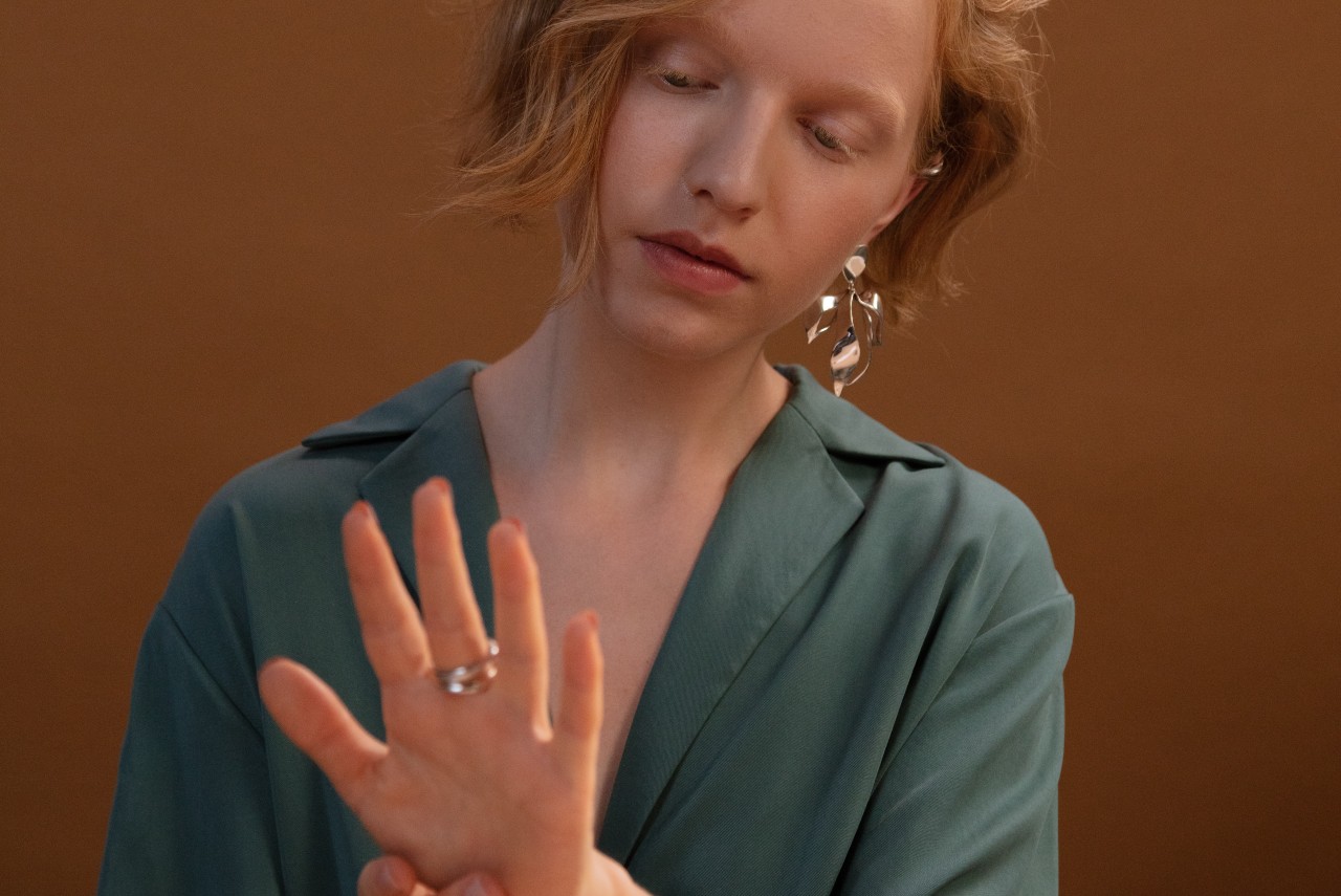 A red-headed woman admires a silver ring that matches her earrings in front of a solid brown background
