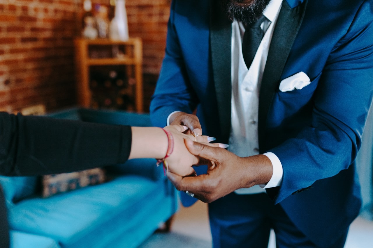 A man slips a dainty engagement ring onto a woman’s manicured finger and inspects it