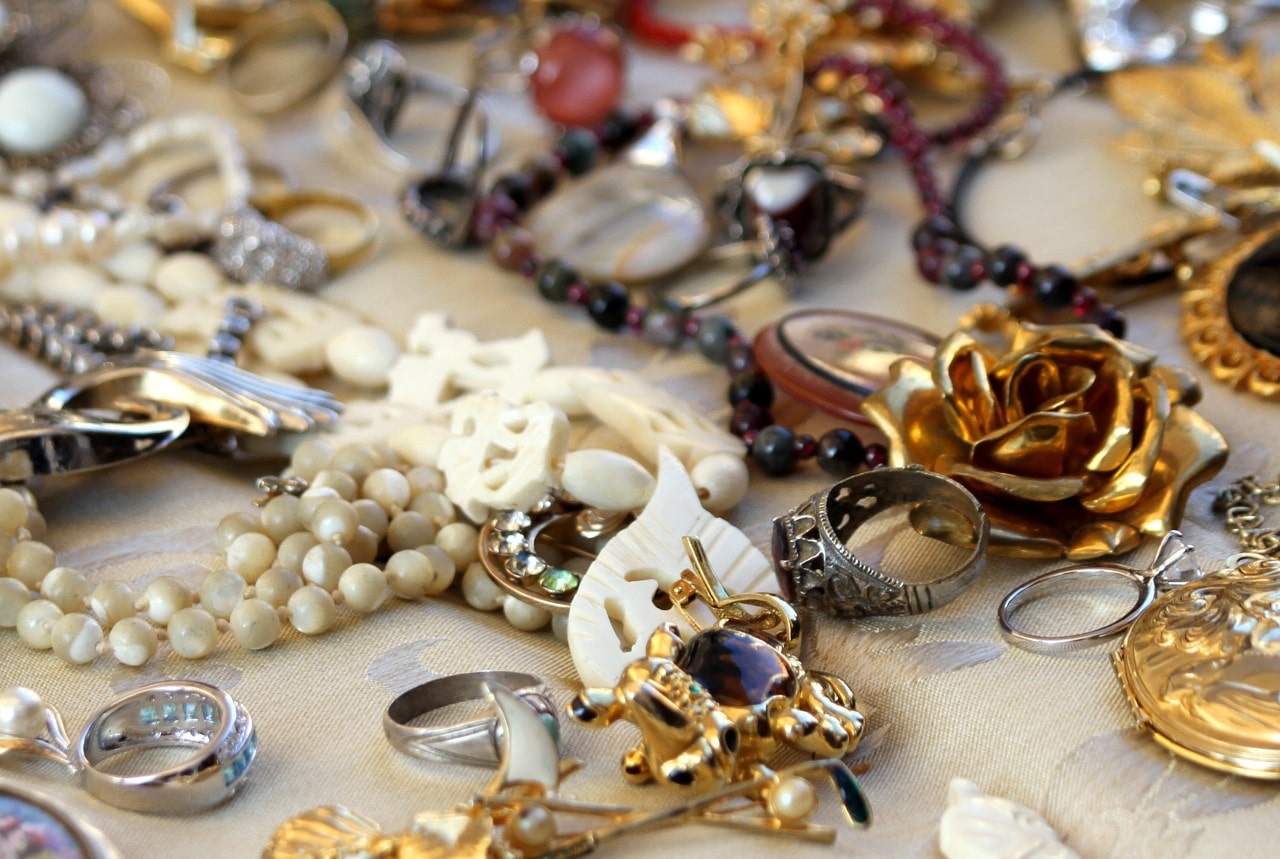 A collection of jewelry of all types, gemstones, and precious metals is messily displayed on a tan cotton fabric