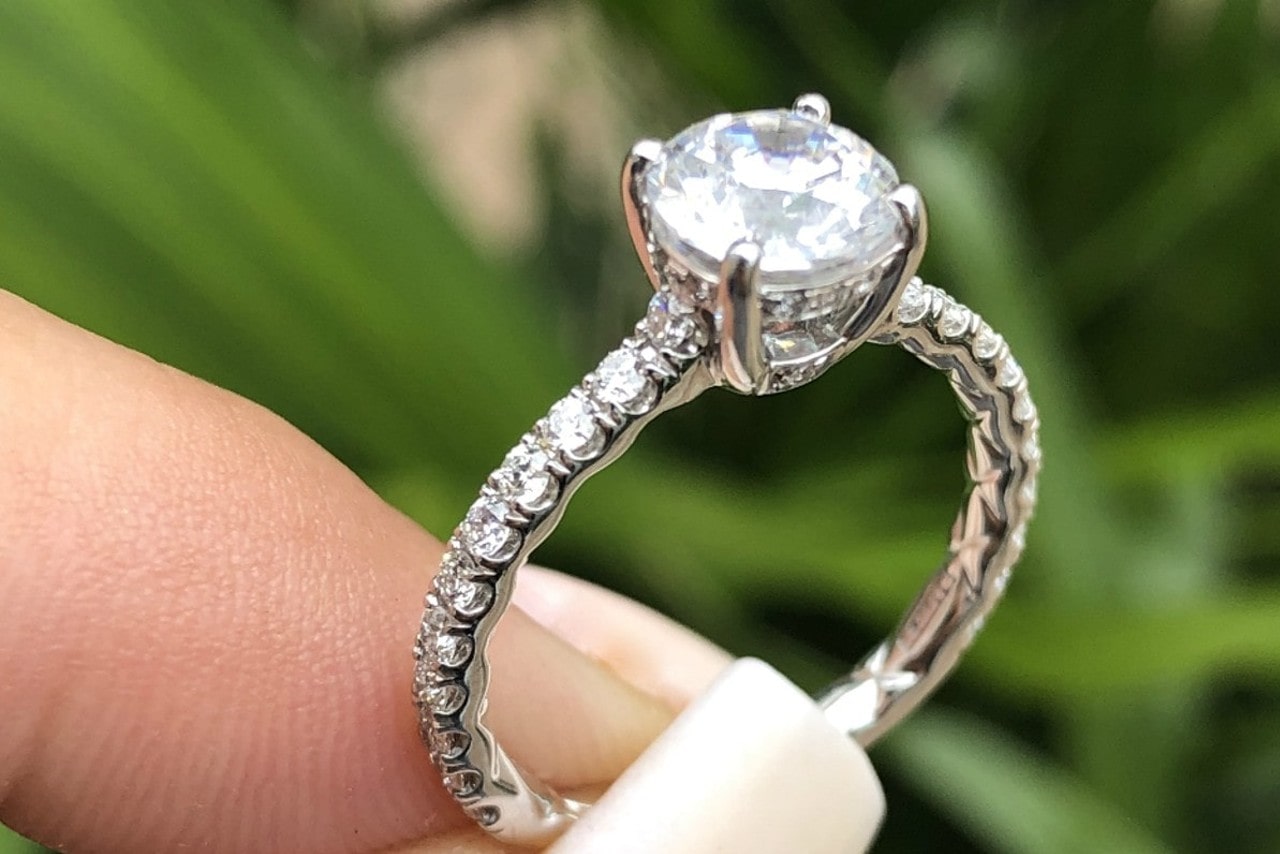 A woman with acrylic nails holds her platinum side stone diamond engagement ring during a tropical hike