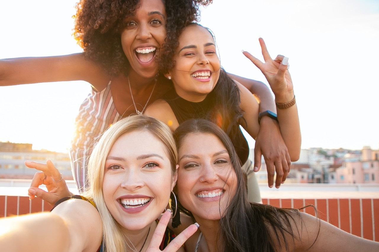 Four fashionable friends taking a selfie together on a rooftop during golden hour before a sunset together at dinner