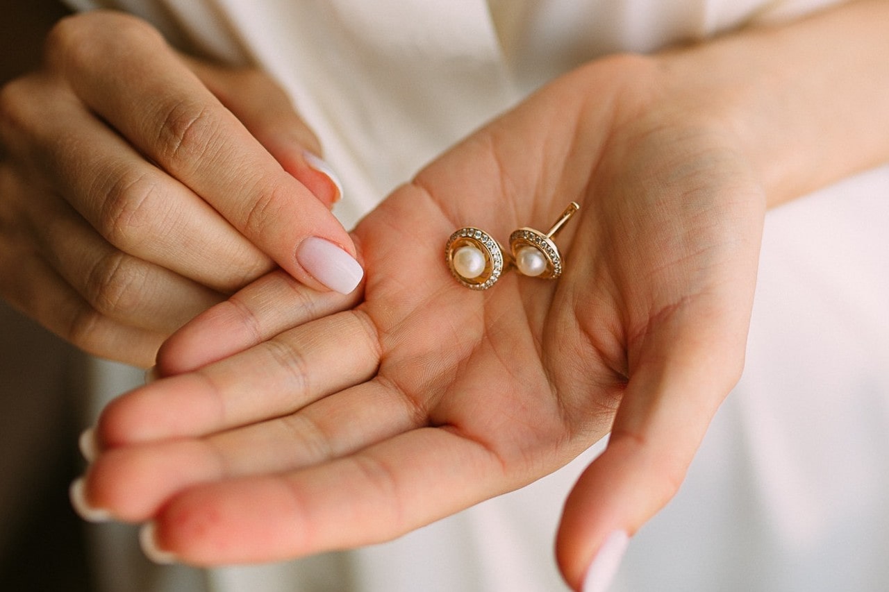 A woman with manicured nails holds a pair of broken pearl earrings in her palm