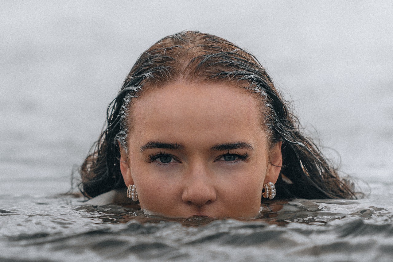 A woman goes swimming in the ocean with two pairs of chunky pearl hoop earrings