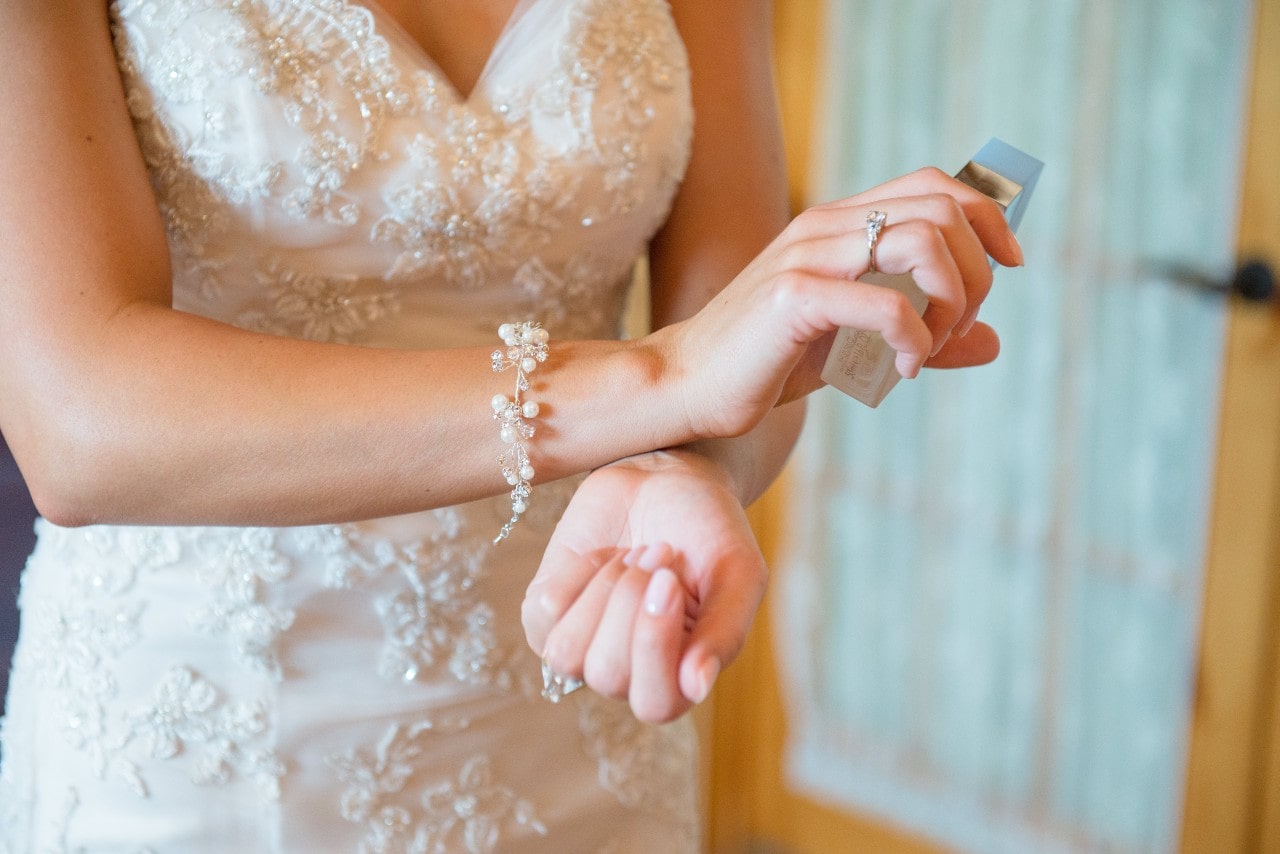 A bride rubs her perfume oil on her wrist before securing her pearl bracelet while she is getting ready for her ceremony