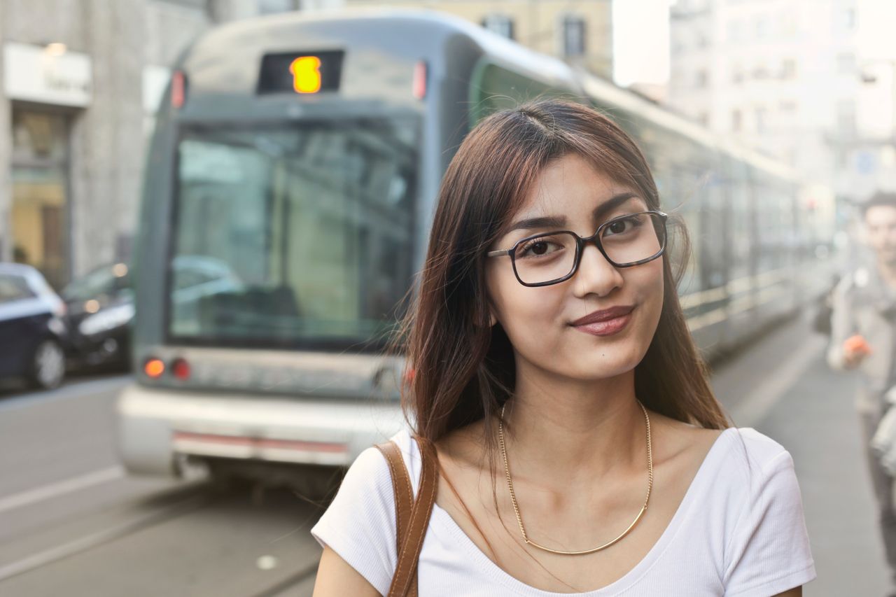 A woman wears glasses and a necklace out in public during a busy weekday on the streets