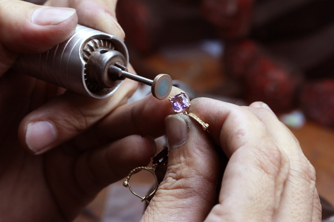 A jeweler polishes an amethyst stone on a pair of hoop earrings as routine maintenance