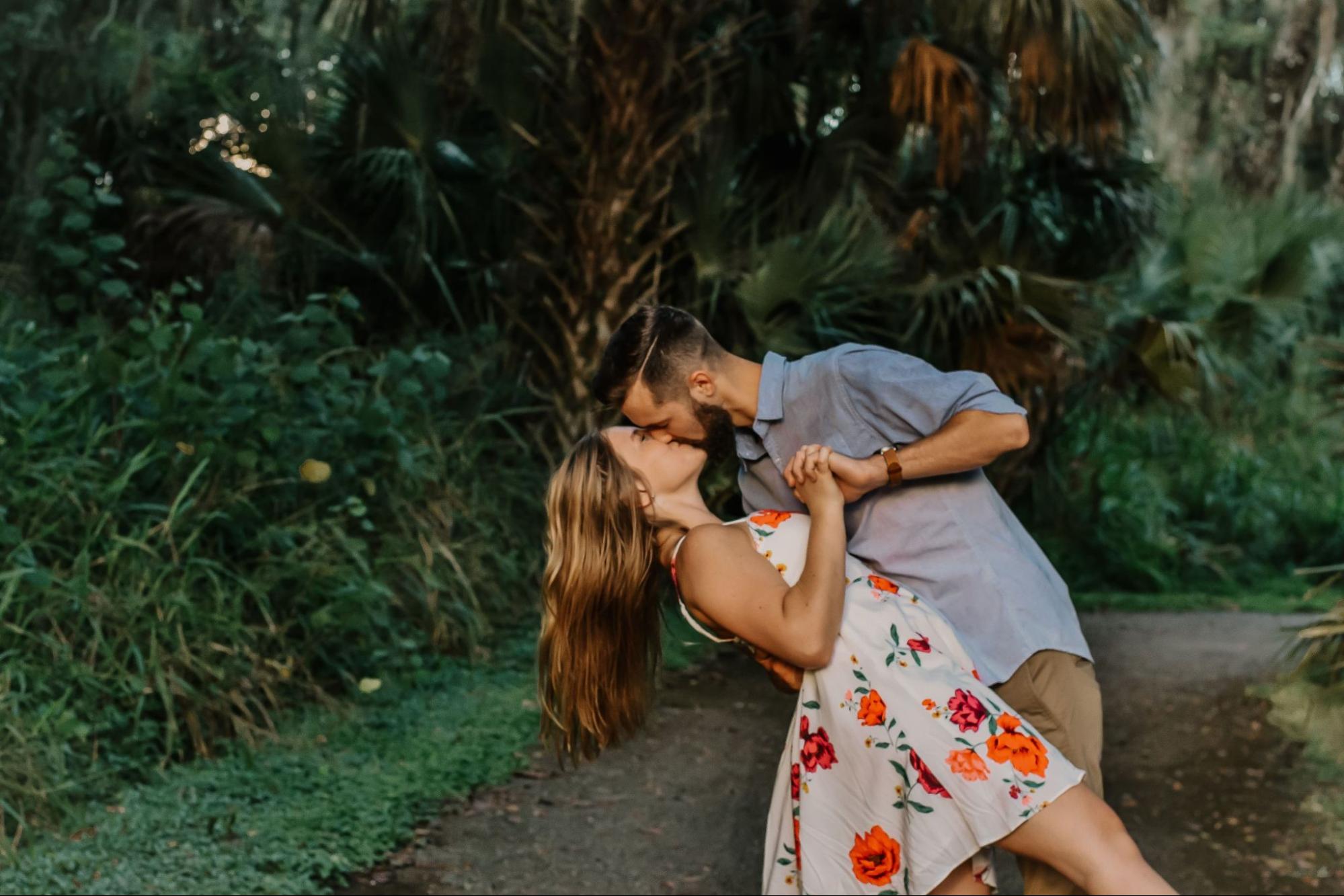 An engaged couple kisses on a narrow road in a tropical environment