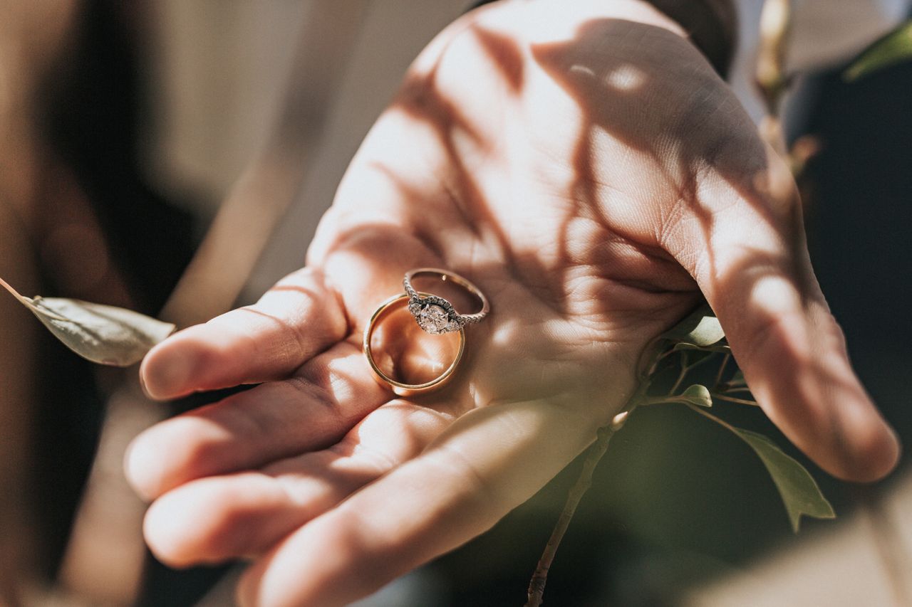 A lab-grown diamond engagement ring and wedding band sit in a man’s palm