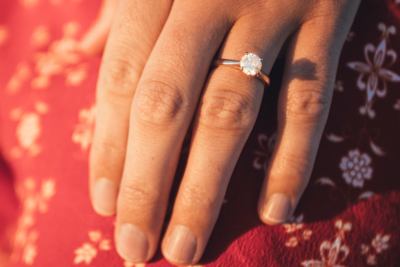 A woman wearing a red floral dress shows off a gold solitaire engagement ring