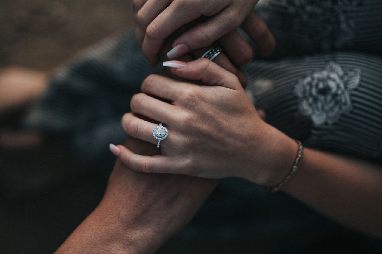 A woman wearing an oval-cut diamond engagement ring rests her hands on her partner’s