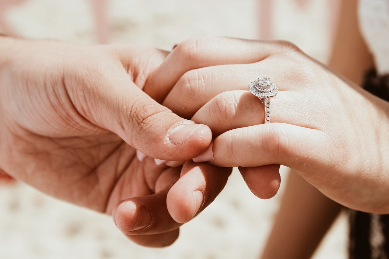A woman with a halo engagement ring holds her lover’s hand
