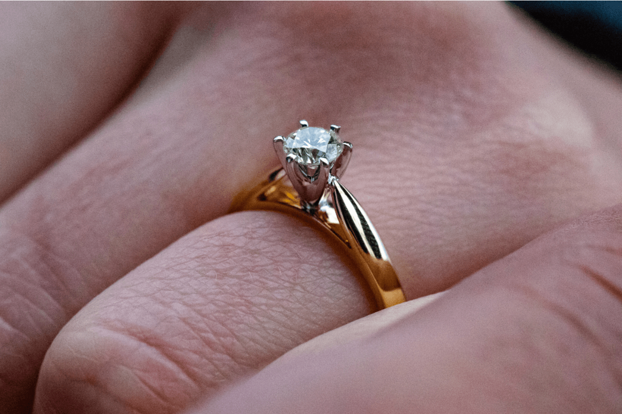 A closeup of a yellow gold solitaire engagement ring on a woman’s finger