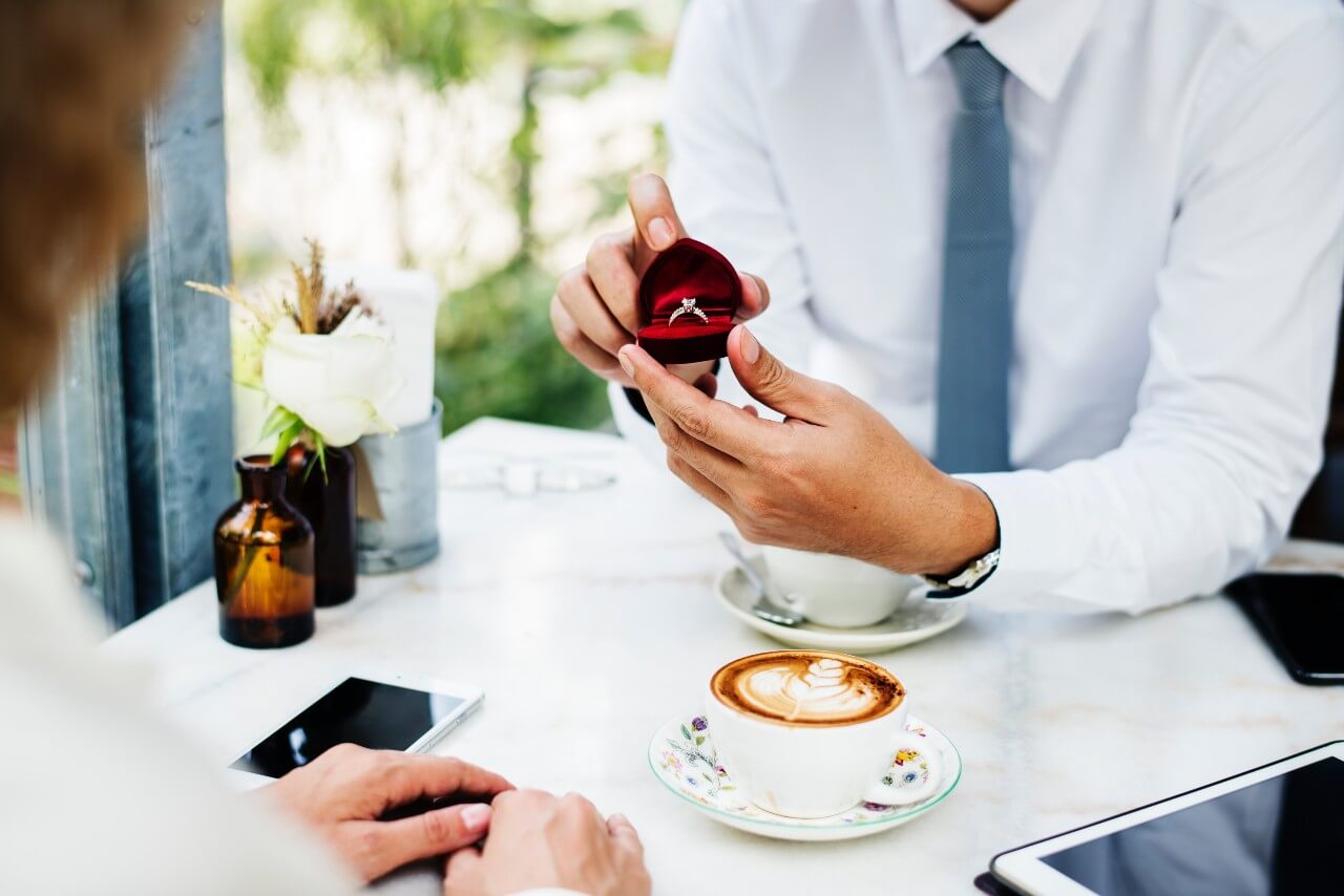 A man proposes with an engagement ring while sitting outside at a coffee shop